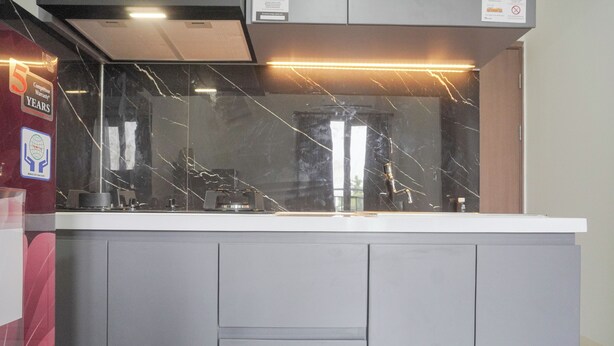 A modern kitchen with a marble backsplash, stainless steel appliances, and a grey cabinetry. - Best Choice and Homey 2BR Podomoro Golf View Apartment (Gunung Putri)