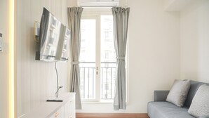 Ein modernes Wohnzimmer mit grauem Sofa, einem flachbildfernseher an der Wand und einem Fenster mit Vorhängen.