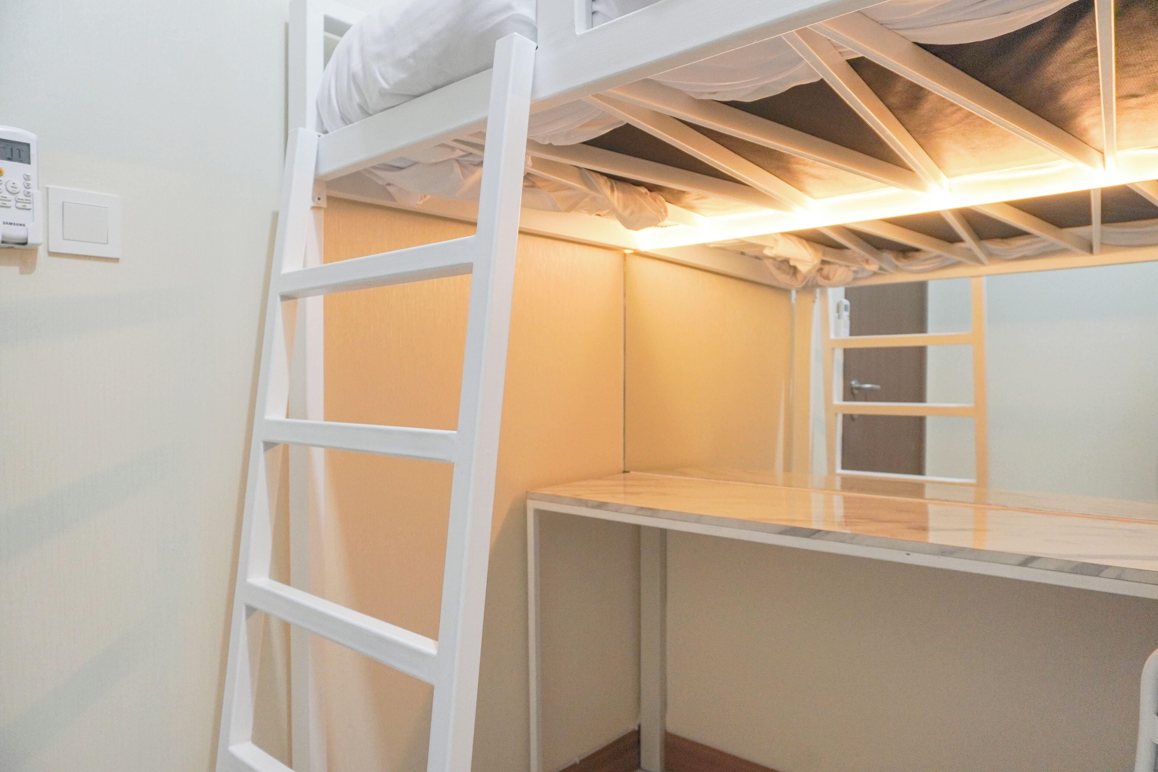 Un lit superposé avec une échelle, une table de chevet et un luminaire fixé au mur.