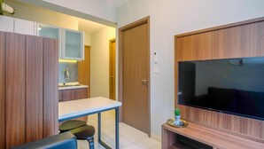 Un espacio habitable compacto con kitchenette, comedor y televisor montado en la pared.
