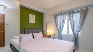 Habitación de hotel con cama, escritorio, silla, espejo y ventana con cortinas.