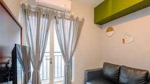 Una sala de estar con un sofá de cuero negro, una televisión y cortinas grises.