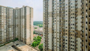 A high-rise residential building with multiple balconies, a parking area, and a view of a cityscape. - Warm and Cozy Living Studio Apartment Podomoro Golf View (Gunung Putri)