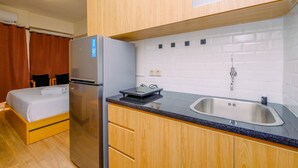A compact kitchen with a refrigerator, a sink, and wooden cabinets. - Warm and Cozy Living Studio Apartment Podomoro Golf View (Gunung Putri)