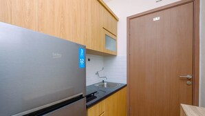A compact kitchen with a stainless steel refrigerator, wooden cabinets, a sink, and a wooden door. - Warm and Cozy Living Studio Apartment Podomoro Golf View (Gunung Putri)