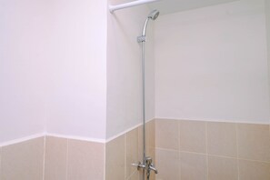 A corner of a bathroom with a shower, a white wall, and beige tiles.