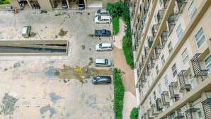 An aerial view of a parking lot with several cars, a pedestrian pathway, and a multi-story residential building with balconies. - Warm and Cozy Living Studio Apartment Podomoro Golf View (Gunung Putri)