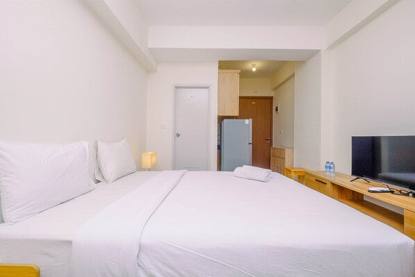 A hotel room with a large bed, a TV, a wooden desk, and a door leading to a bathroom.