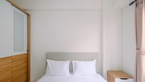 A neatly made bed with white bedding, a wooden headboard, a small bedside table with drawers, and a curtain on the right.