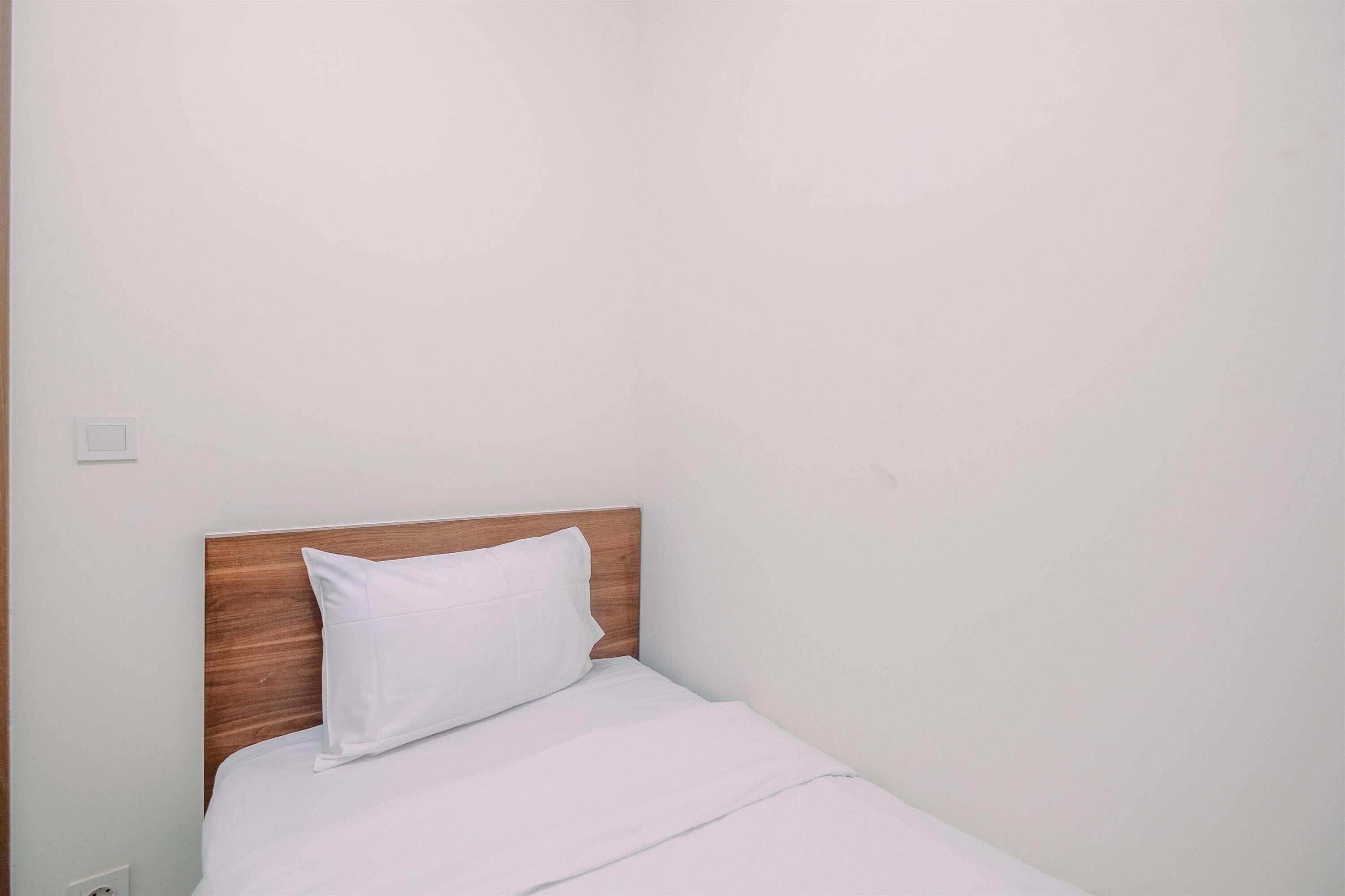 A single bed with a wooden headboard and white bedding in a room with plain white walls.