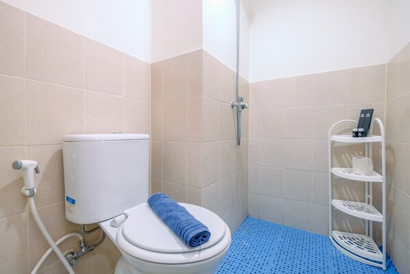 A bathroom with a toilet, a shower, and a white shelf with toiletries. - Comfy and Tidy 1BR at Podomoro Golf View Apartment (Gunung Putri)