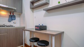A modern kitchen with wooden cabinets, a gas stove, and a countertop. There are two black stools and a small table with a bag on it. - Minimalist and Cozy Stay 2BR at Podomoro Golf View Apartment (Gunung Putri)