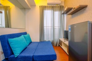 A room with a blue sofa, a television, and a refrigerator. - Minimalist and Cozy Stay 2BR at Podomoro Golf View Apartment (Gunung Putri)