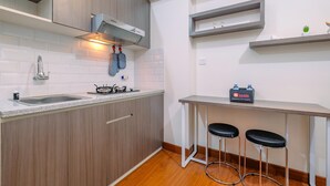 A modern kitchen with wooden cabinets, a built-in stove, a sink, and a bar area with stools. - Minimalist and Cozy Stay 2BR at Podomoro Golf View Apartment (Gunung Putri)