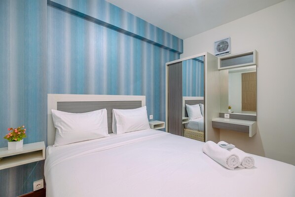A hotel room with a bed, a nightstand, a mirror, and a wall-mounted air conditioner. - Minimalist and Cozy Stay 2BR at Podomoro Golf View Apartment (Gunung Putri)