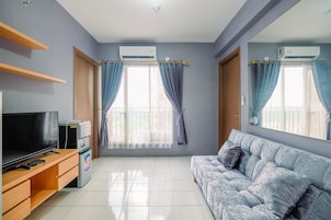 A living room with a flat-screen TV, a small refrigerator, a sofa, and a window with curtains.