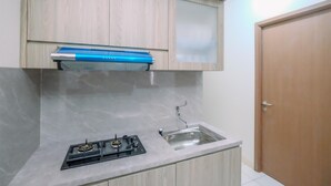 A kitchen with a gas stove, a stainless steel sink, wooden cabinets, and a blue range hood. - Comfort Stay 2BR at Podomoro Golf View Apartment (Gunung Putri)