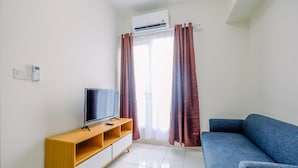 A living room with a blue sofa, a wooden TV stand, and a flat-screen TV. - Comfort Stay 2BR at Podomoro Golf View Apartment (Gunung Putri)