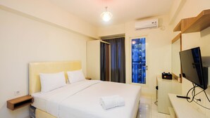 Una habitación de hotel con cama, televisor, escritorio y aire acondicionado.