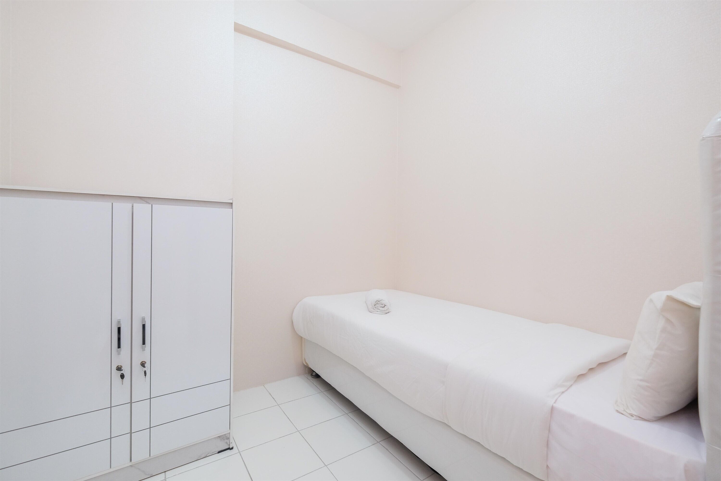 A small, single-bed room with a white wardrobe and a plain wall.