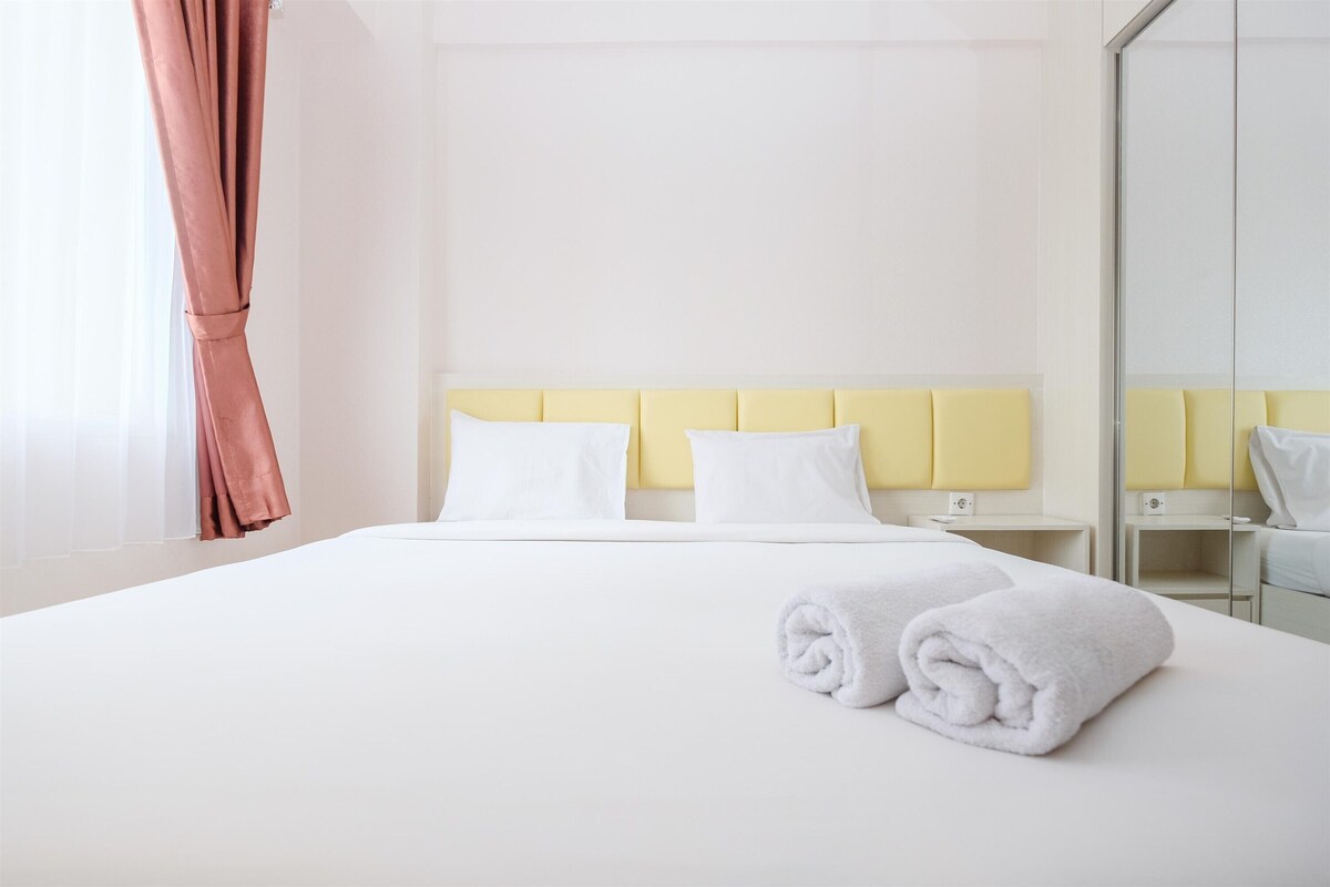 A hotel room with a bed, two bedside tables, a mirror, and a window with curtains.