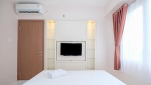 Ein Hotelzimmer mit Bett, einem an der Wand montierten Fernseher, einer Tür und einem Vorhangfenster.