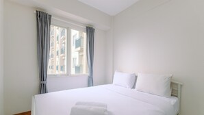 A hotel room with a large bed, white bedding, a neatly folded towel, and a window with curtains. - Simply Look and Tidy 2BR at Podomoro Golf View Apartment (Gunung Putri)