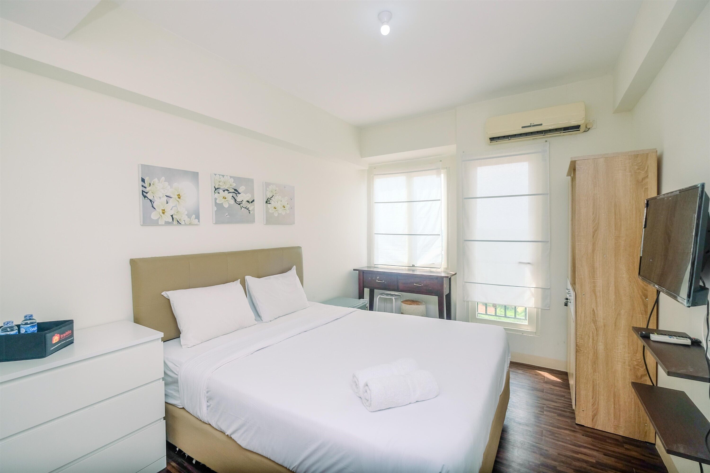 A hotel room with a bed, a desk, a TV, and artwork on the wall.