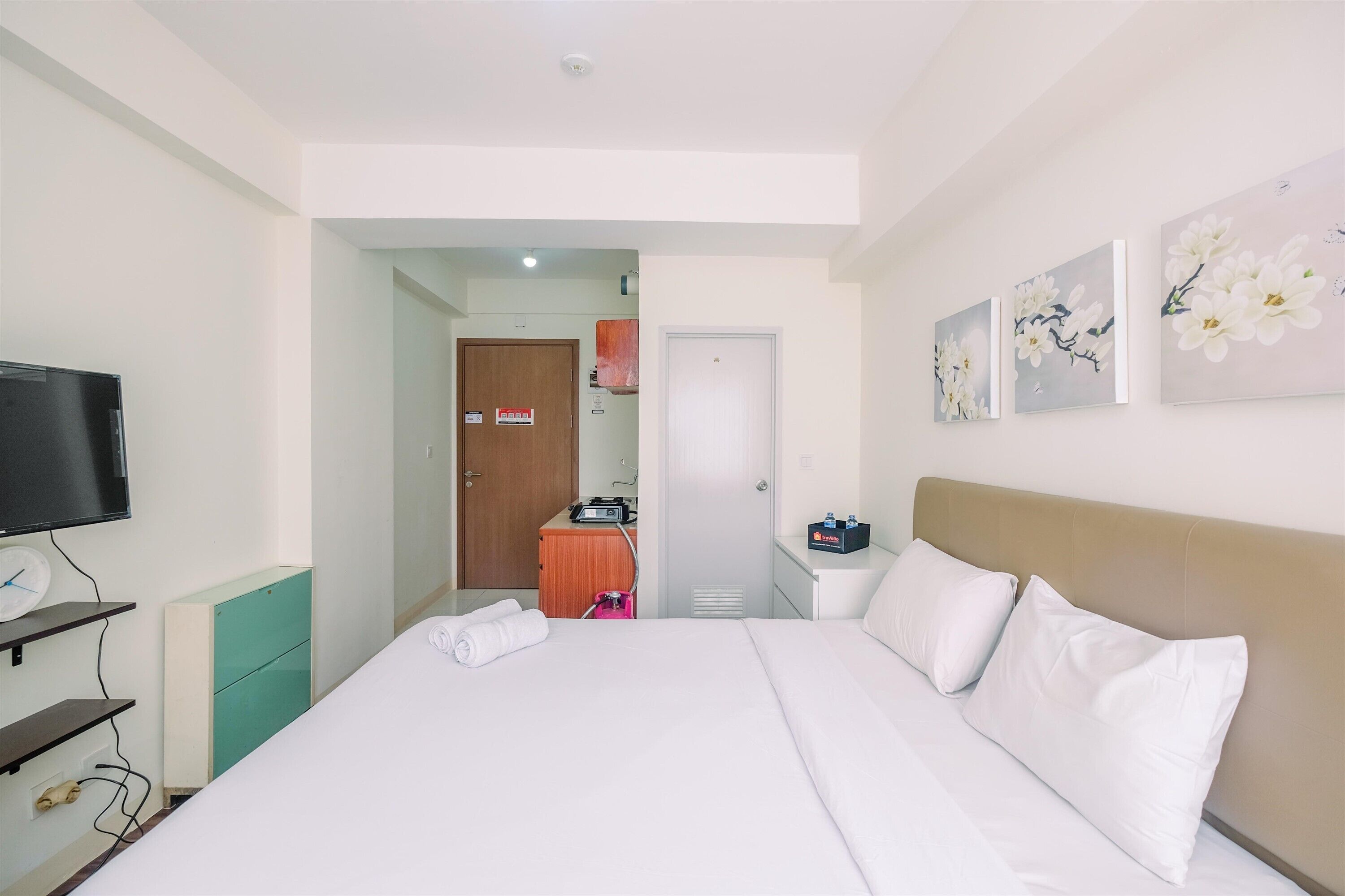 A hotel room with a bed, a television, a desk, and artwork on the wall.