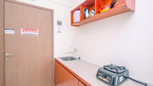 A kitchen with a wooden door, a stainless steel sink, a countertop with a gas stove, and a wooden shelf above the sink. - Comfortable and Lovely Studio Podomoro Golf View Apartment (Gunung Putri)