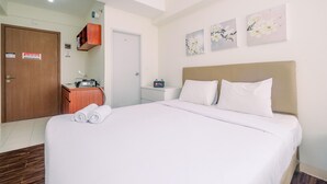 A hotel room with a large bed, a wooden wardrobe, a small desk with a radio, and wall-mounted artwork. - Comfortable and Lovely Studio Podomoro Golf View Apartment (Gunung Putri)