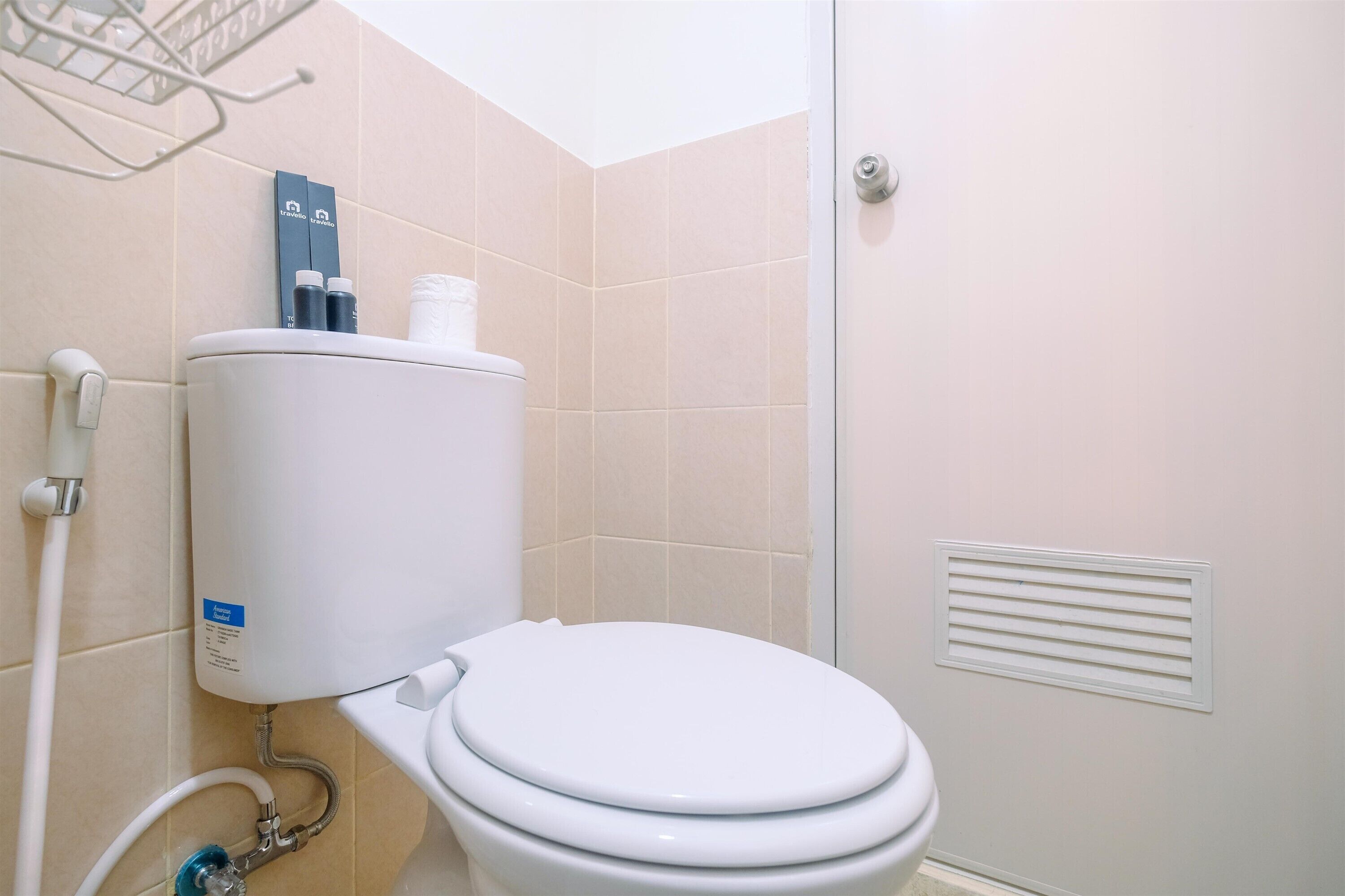 A modern bathroom with a white toilet, beige tiles, a water heater, and a shower area.