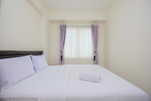 A neatly made bed with white linens and a rolled towel, a headboard, and a window with sheer white curtains and purple drapes. - Comfort 2BR at 6th Floor Podomoro Golf View Apartment (Gunung Putri)