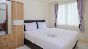 A neatly made bed with white linens and two rolled towels, a wooden wardrobe with a mirror, and a window with purple curtains. - Comfort 2BR at 6th Floor Podomoro Golf View Apartment (Gunung Putri)