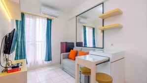 A modern hotel room with a glass table, a sofa with orange cushions, a TV, and a large mirror. - Best Deal and and Cozy 2BR Podomoro Golf View Apartment (Gunung Putri)