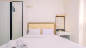 A neatly made bed with white linens and pillows, a bedside table with a lamp, and a mirror on the wall. - Best Deal and and Cozy 2BR Podomoro Golf View Apartment (Gunung Putri)
