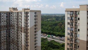A high-rise residential building with multiple balconies and a view of a busy road and greenery in the background. - Comfort 2BR at 28th Floor Podomoro Golf View Apartment (Gunung Putri)
