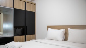 A hotel room with a bed, white linens, a wooden headboard, a large mirror, and a wardrobe with a black panel. - Comfort 2BR at 28th Floor Podomoro Golf View Apartment (Gunung Putri)