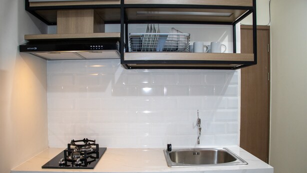 A kitchen with a gas stove, stainless steel sink, white tiled backsplash, and wooden cabinets. - Comfort 2BR at 28th Floor Podomoro Golf View Apartment (Gunung Putri)