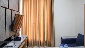 A room with a flat-screen TV mounted on the wall, a desk with a computer and a projector, a sofa, and a curtain. - Comfort 2BR at 28th Floor Podomoro Golf View Apartment (Gunung Putri)
