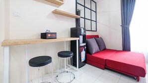 A compact living space with a red sofa, a small bar area with stools, a refrigerator, and a water dispenser.