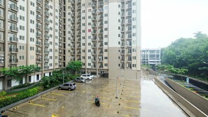 A high-rise residential building with multiple balconies and a parking area.