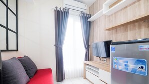 A compact room with a red sofa, a flat-screen TV, a refrigerator, and a wooden wall.