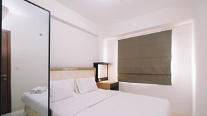 A hotel room with a bed, bedside table, lamp, and window with blinds. - Simple and Cozy Living 2BR at Podomoro Golf View Apartment (Gunung Putri)