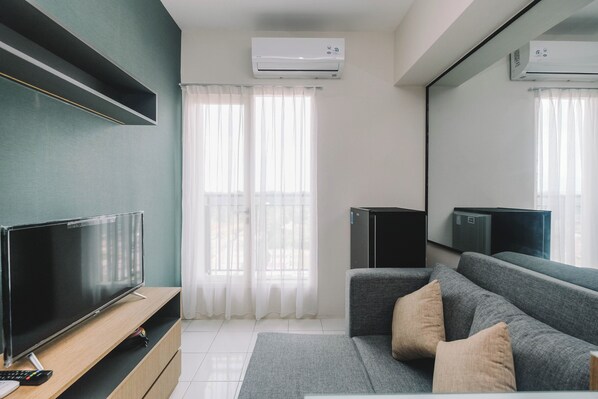 Un salon moderne avec un téléviseur à écran plat posé sur un meuble en bois, un canapé gris agrémenté de coussins et deux unités de climatisation fixées au mur.