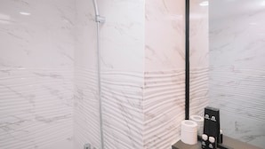 A bathroom with a shower, marble walls, a mirror, and toiletries. - Simple and Cozy Living 2BR at Podomoro Golf View Apartment (Gunung Putri)