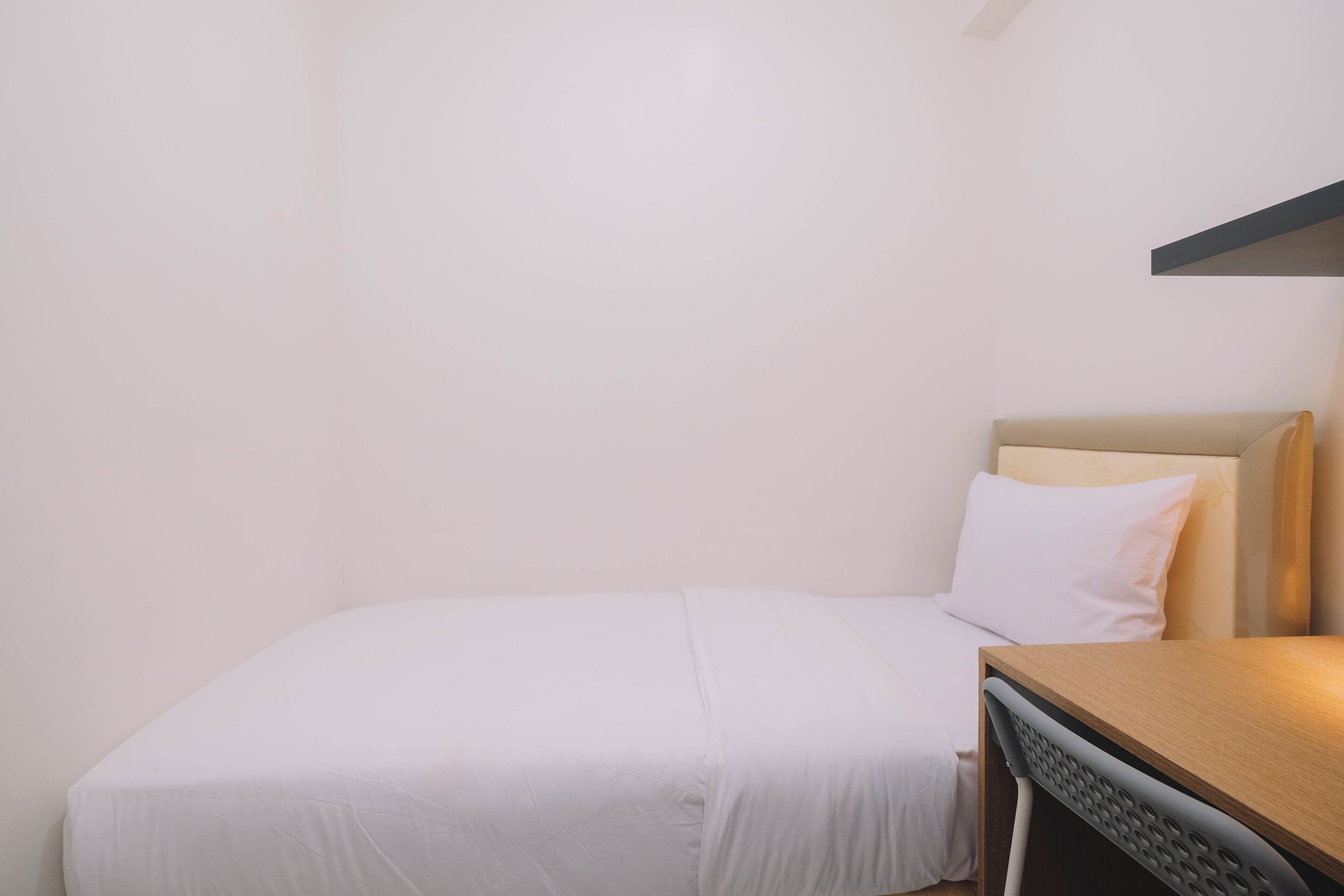 A single bed with a white mattress and pillow, a wooden headboard, and a small bedside table with a lamp.