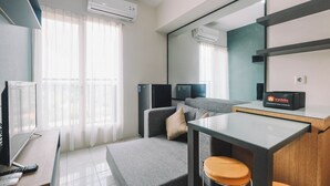 A modern hotel room with a sofa, a small table, a TV, and a minibar. - Simple and Cozy Living 2BR at Podomoro Golf View Apartment (Gunung Putri)