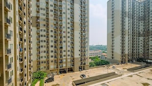 A high-rise residential building with multiple balconies, a parking area, and a view of the surrounding landscape. - Contemporary Studio at Podomoro Golf View Apartment (Gunung Putri)
