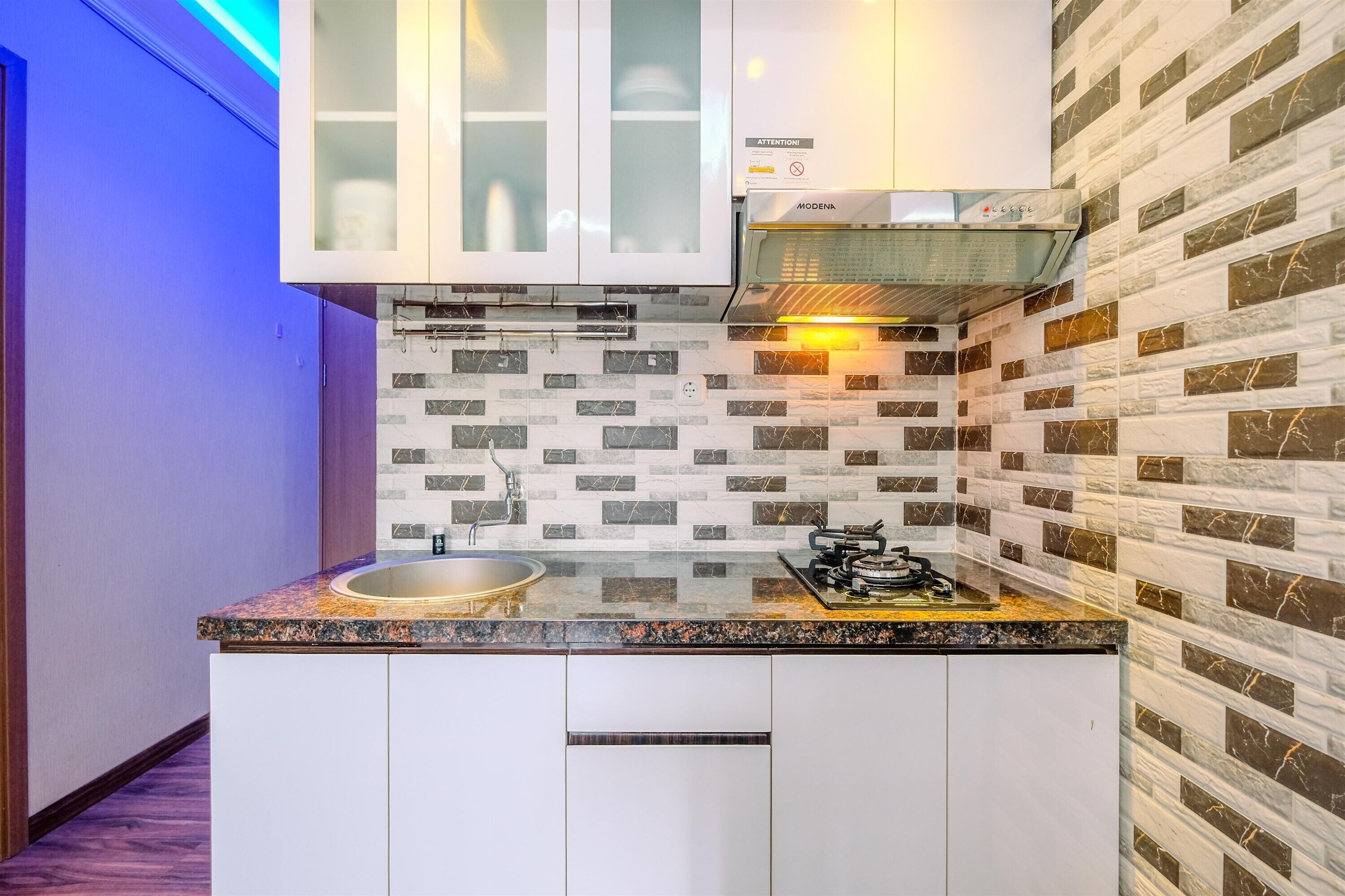 A compact kitchen with white cabinets, a granite countertop, a stainless steel sink, and a built-in range hood.